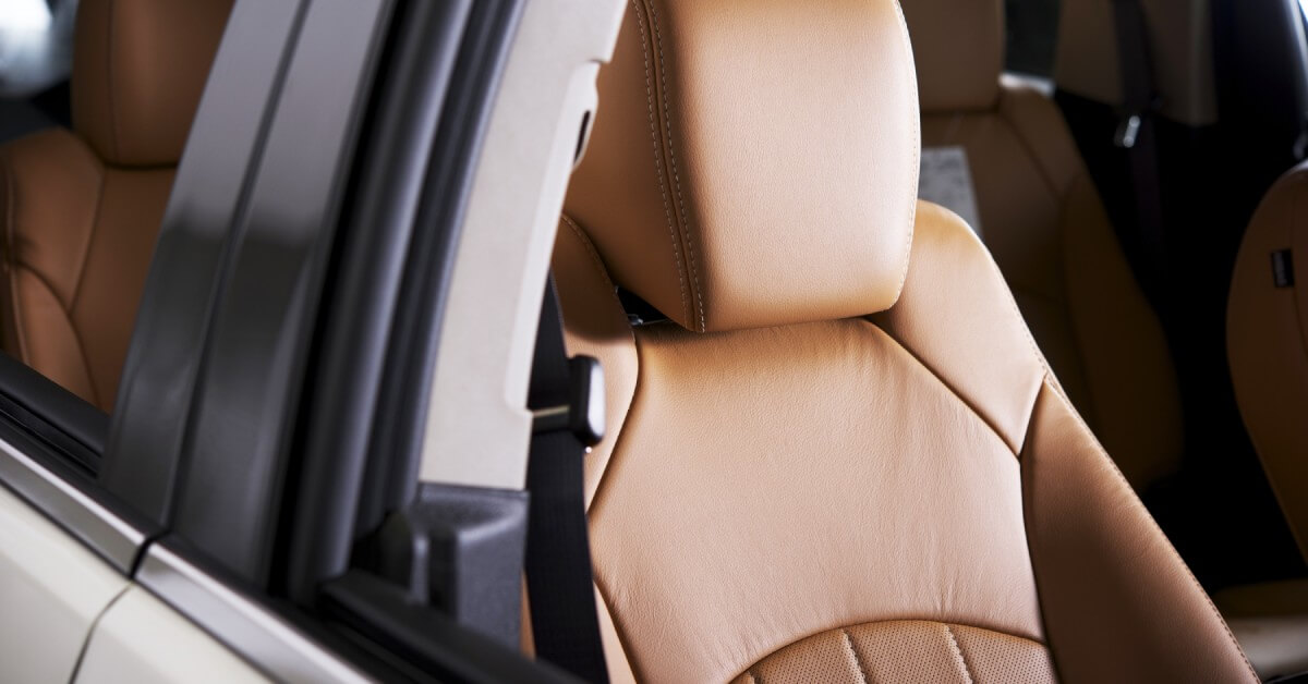 A white sedan's empty interior with two rows of seats with warm brown leather upholstery. The car's windows are fully down.