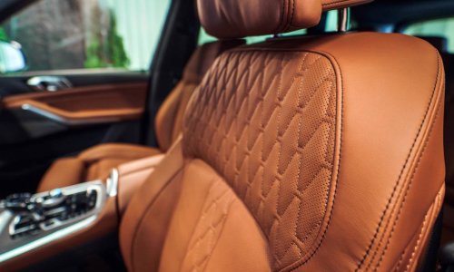 A close-up of warm brown leather seat cover with a matching center console in a sedan with chrome accents.