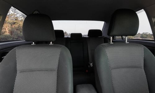 A sedan's interior contains grey upholstery. A forest is visible outside of the vehicle's side and rear windows.