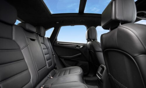 Rear seats in a luxury sedan with black leather upholstery. A blue sky with few clouds can be seen from the windows.