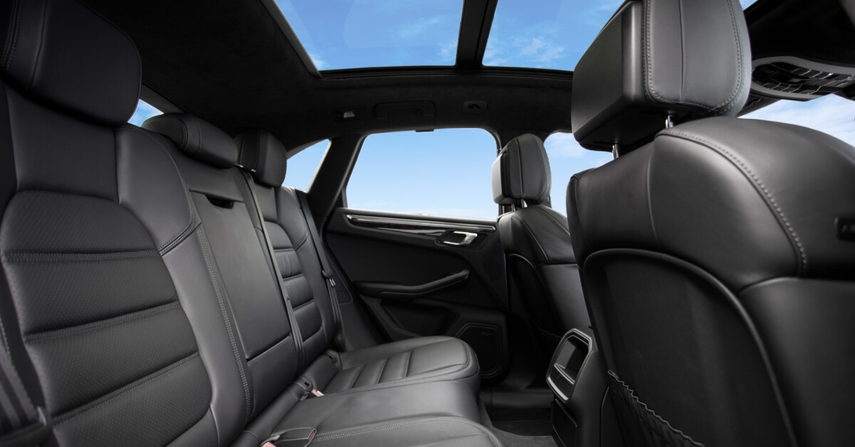 Rear seats in a luxury sedan with black leather upholstery. A blue sky with few clouds can be seen from the windows.