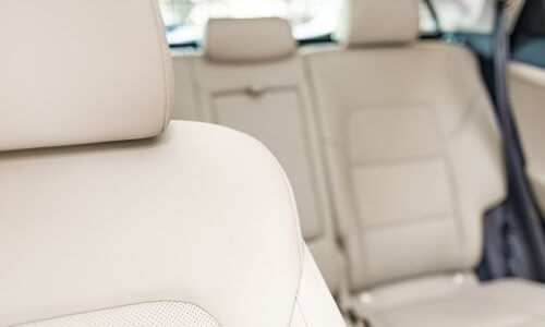 A close-up of a sedan passenger seat made from off-white leather with the back seats in the blurred background.