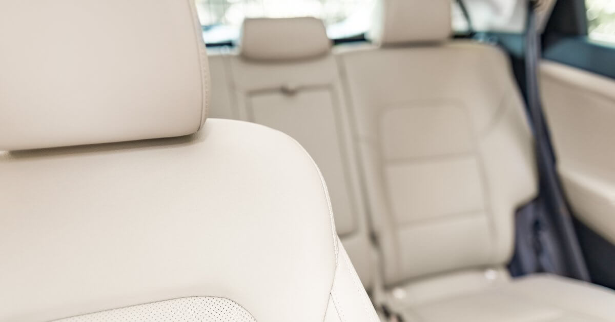 A close-up of a sedan passenger seat made from off-white leather with the back seats in the blurred background.