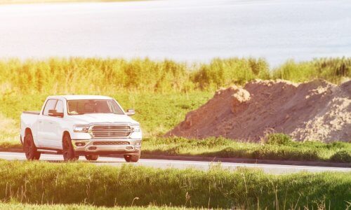 A clean white pickup truck driving on a narrow road lined with tall grass by a body of water. It is all tinted yellow.