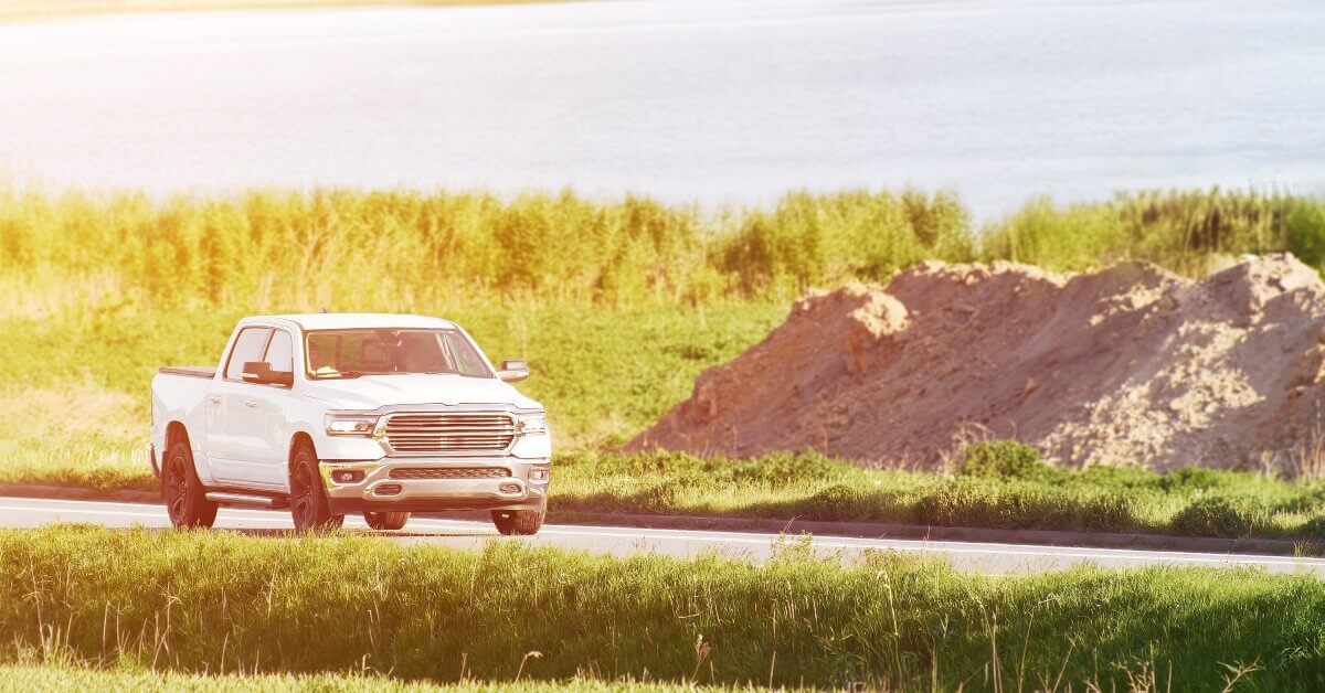 A clean white pickup truck driving on a narrow road lined with tall grass by a body of water. It is all tinted yellow.